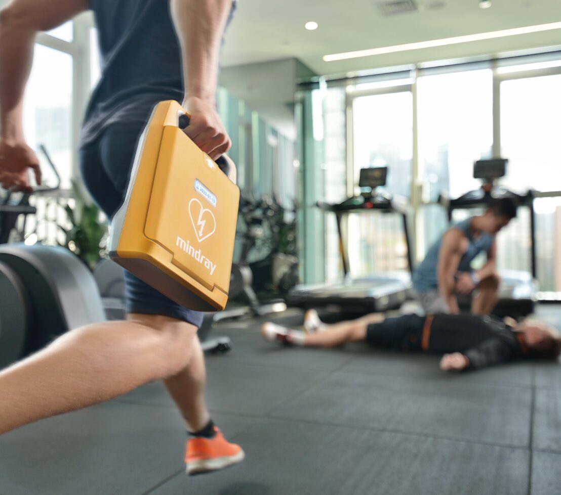 Person springer med hjärtstartare i gym mot medvetslös person